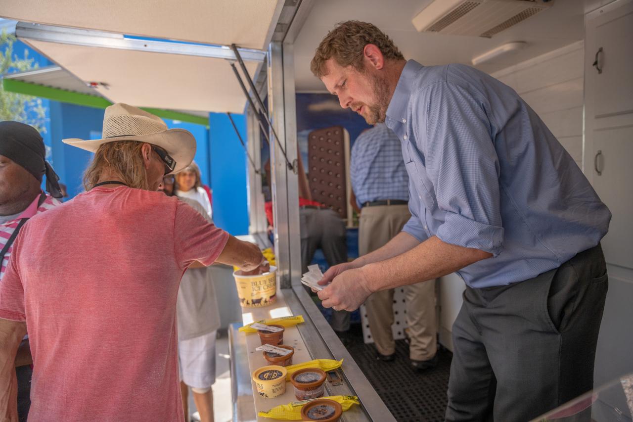 A man in the refrigerated Blue Bell Ice Cream trailer hands out spoons for the displayed ice cream servings as a guest at SVdP's Phoenix Dining Room reaches for one.