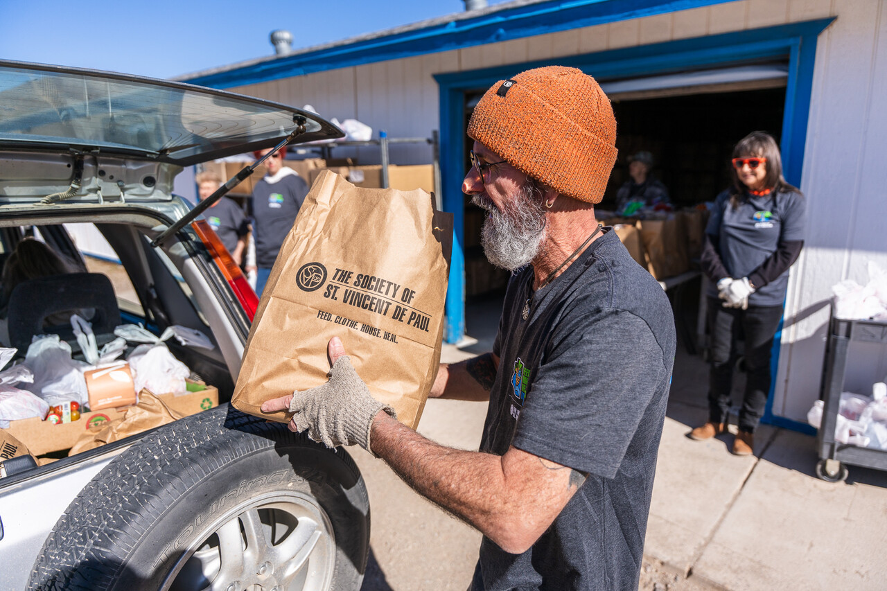 A volunteer loads a food bag into a guest's car.